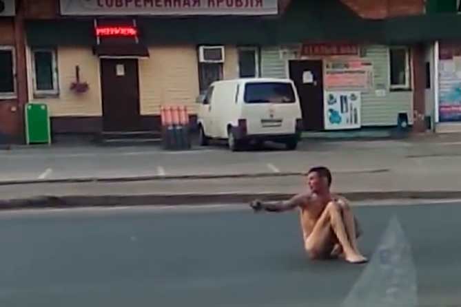 голый мужчина сидит на проезжей части