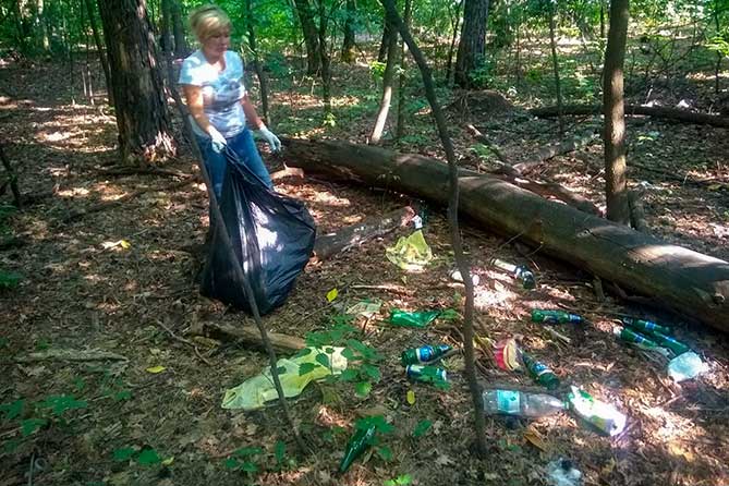 женщина убирает бутылки в лесу